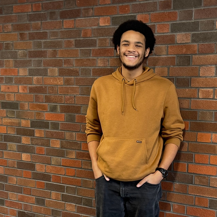 Student smiling while standing by a brick wall. 