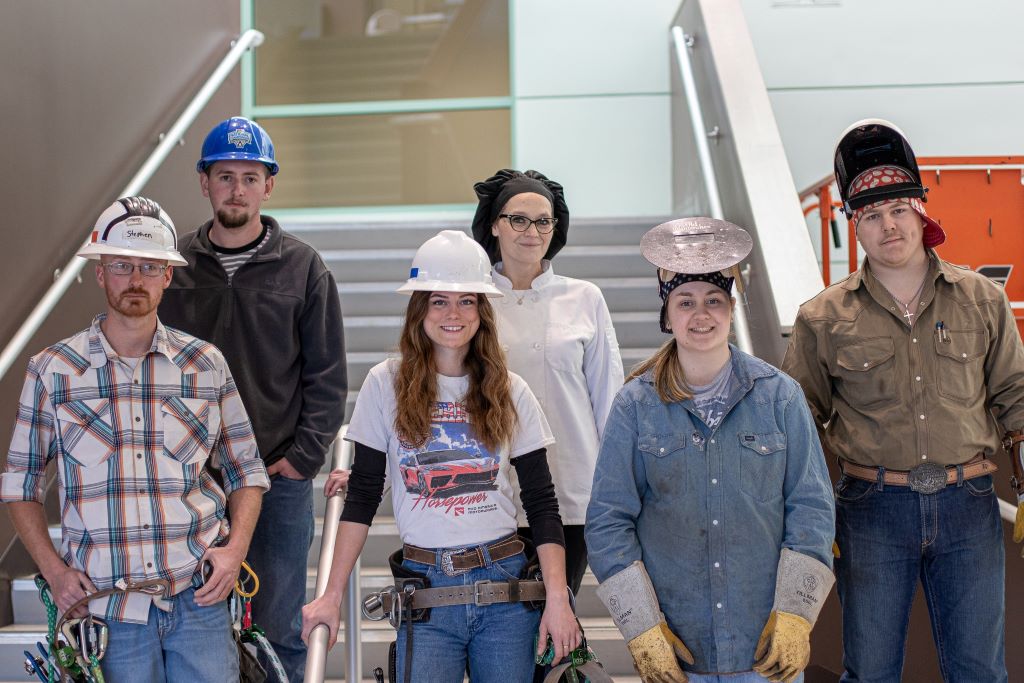  Students at ACTC who completed internships in their programs. Each student is wearing gear for their program including: Welding helmets,  lineman climbing equipment and hardhat, a chef smock and hat, etc.