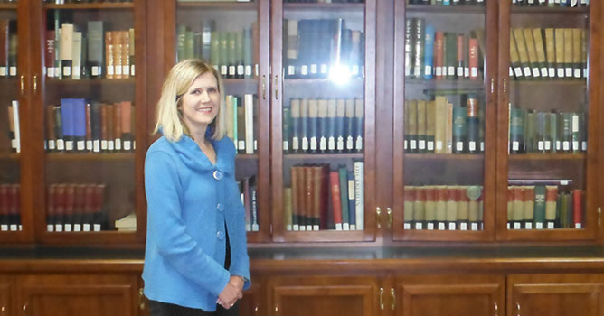 Disabled Student Sevices Coordinator and advisor Heather Shelton stands in front large oak bookcase in the meeting room at the Masbach Memorial Library.