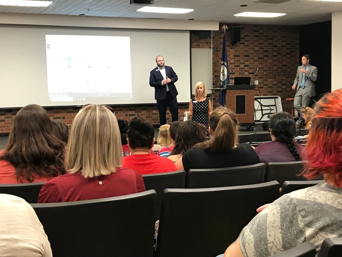 A speaker and host standing in front of an audience in the Teleconference room on College Drive Campus