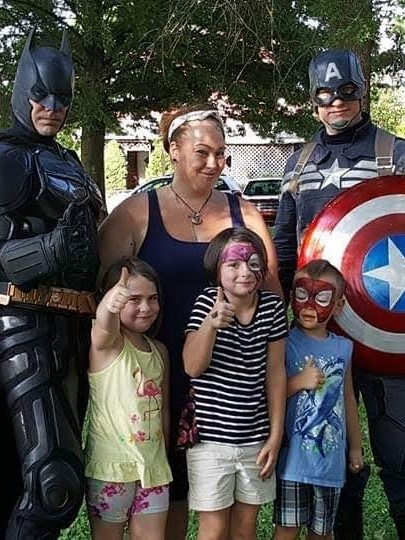 A Ready to Work student posing and her 3 children posing with Batman and Captain America
