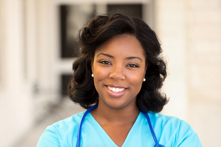 The smiling face of a Nursing Assistant student wearing scrubs and a stethoscope. 