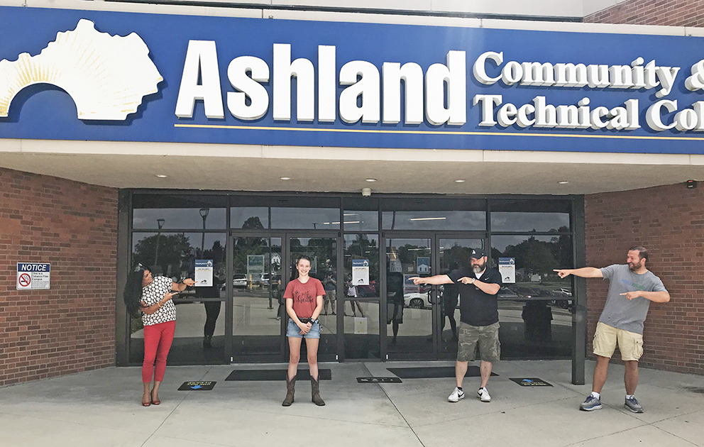 Four people smiling and standing outside of a college building